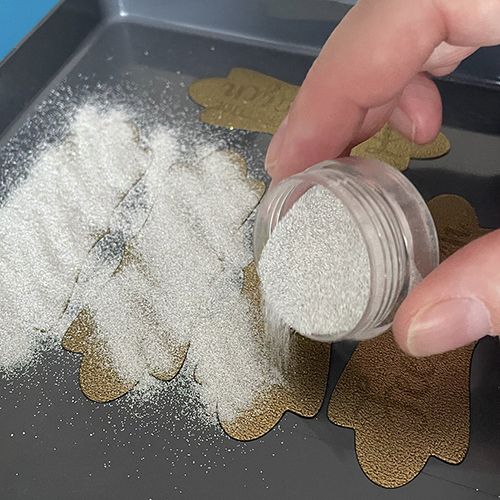 Strooi embossing powder over de items in het bakje.